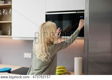 Woman Using Microwave Oven For Heating Food At Home