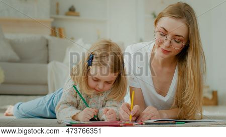 Caucasian Mother Lying Of Floor At Home With Little Small Adopted Child Girl Enjoy Draw Together. Da