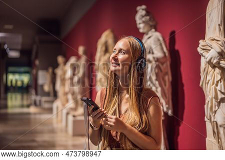 Portrait Of Contemporary Young Woman Looking At Sculptures And Listening To Audio Guide At Museum Ex
