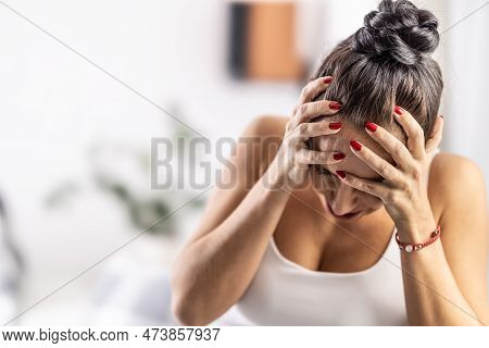 Stressed And Exhausted Woman With Migrene Holds Her Head In The Hands From Distress.