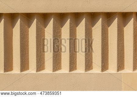 Beige Exterior Stucco Wall With Repeating Details. Rough Surface In The Sun With Shadows. Rough Text