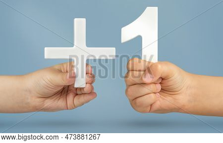 Plus One, Plus Size, Add One Concept. White Number 1 With A Plus In Hand On A Blue Background Close-