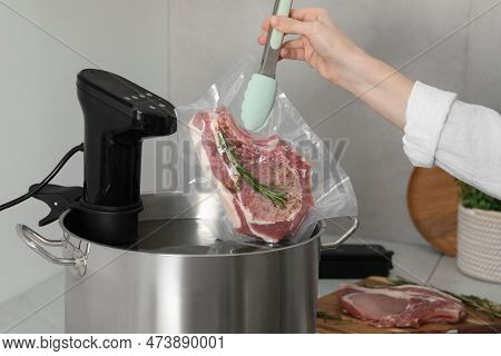 Woman Putting Vacuum Packed Meat Into Pot With Sous Vide Cooker In Kitchen, Closeup. Thermal Immersi