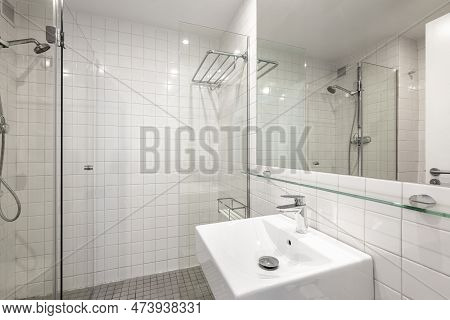 Cozy And Laconic Bathroom With White Tiles, A Sink And Glass-enclosed Shower. Concept Of An Inexpens