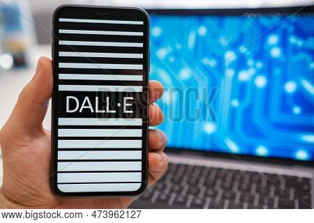 A Mans Hand Holding A Smartphone With Dall E Neural Network Logo On The Screen And A Laptop Displayi