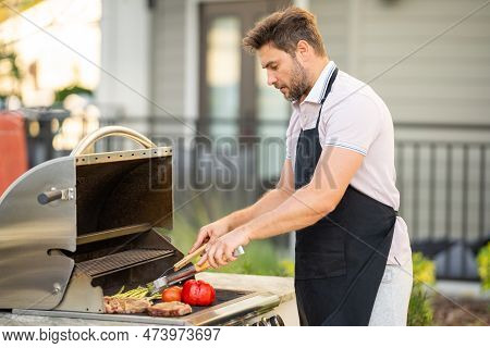Man Cooking Meat On Barbecue In The Backyard Of The House. Handsome Man Preparing Barbecue. Barbecue