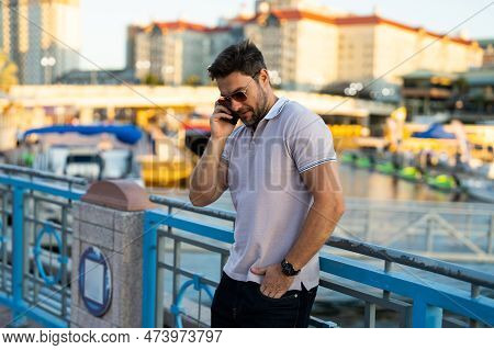 Young Handsome Man In Classik Polo T-shirt Chatting On Phone On The Street. Handsome Confident Styli