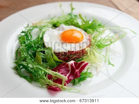 Beef tartar with fried egg and lettuce in plate