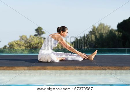 Peaceful brunette in janu sirsasana yoga pose poolside on a sunny day at the spa