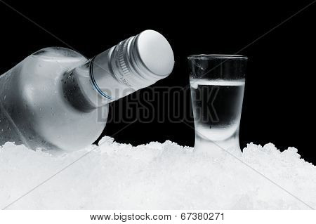 Bottle With Glass Of Vodka Lying On Ice On Black Background