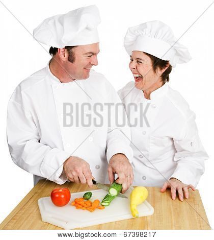 Two chefs working together in the kitchen and laughing as they cut up vegetables. Isolated on white.  