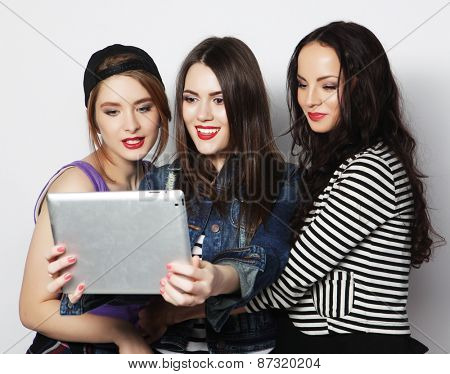Three girls friends taking selfie with digital tablet, studio shot over gray vackground