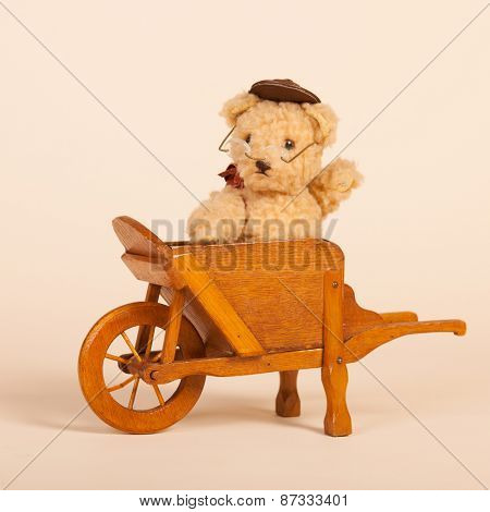 Hand made stuffed funny bear sitting in vintage wheel barrow