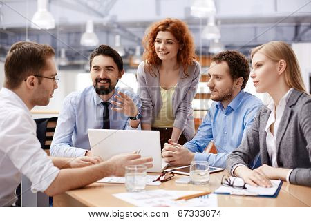 Several business partners looking at their colleague explaining viewpoint at meeting