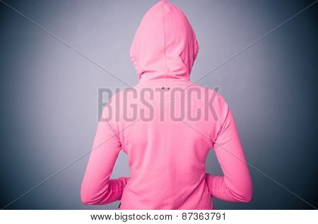 Back view protrait of a woman in pink jacket with hood over gray background