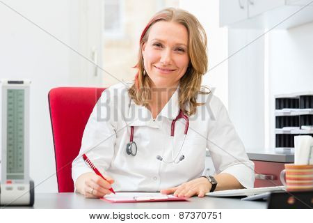 Young gynaecologist writing medical prescription in surgery at desk