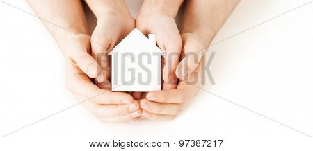 real estate and family home concept - closeup picture of male and female hands holding white blank paper house