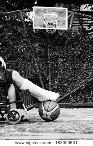 man sitting on wheel chair with broken leg in Plaster cast at basketball court