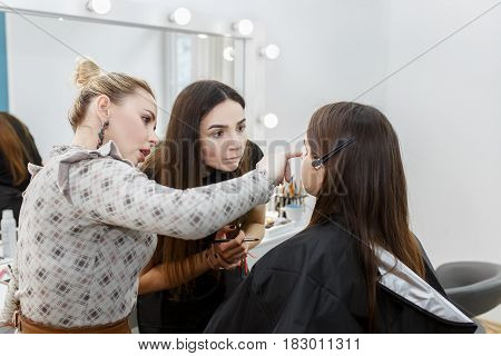 professional makeup teacher training her student girl to become makeup artist. Makeup tutorial lesson at beauty school. Master class. Real people. Visagiste explaining how to apply makeup properly