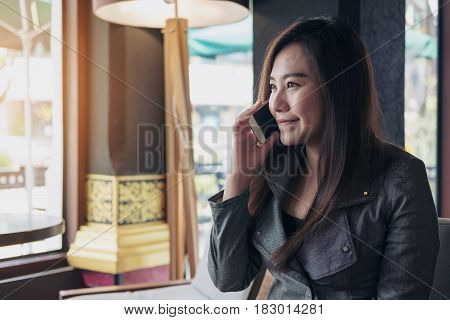 A beautiful Asian woman looking outside window and talking on smart phone in the room