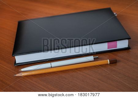 Black Diary, Or Sketchbook With Pen And Pencil On Th Table