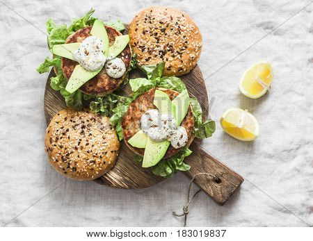 Fish burger. Burgers with tuna avocado and mustard sauce with whole grain homemade buns on wooden cutting board on a light background top view