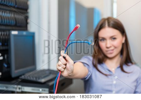Young engineer and businesswoman with the management console holds two colored patch cords And stands between the server racks in the data center