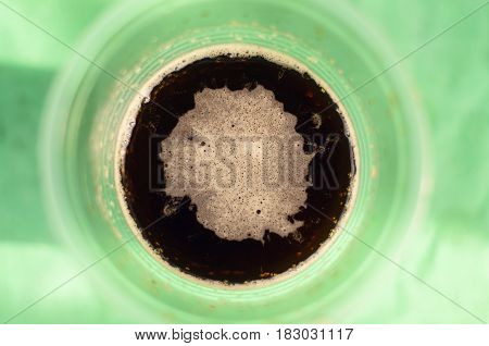 Dark beer (ale) in a plastic cup on the table. Top view. Outdoor vacation concept.