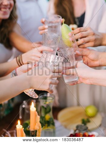 picnic, people, holiday concept - happy young people clink glasses near table with flagon of lemonade and candle, one glass with whole pear instead of lemonade, flagon with lemons, limes, mint leaves