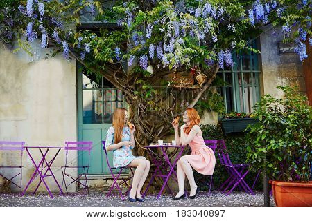Parisian Women Drinking Coffee Together In An Outdoor Cafe With Wisteria In Full Bloom