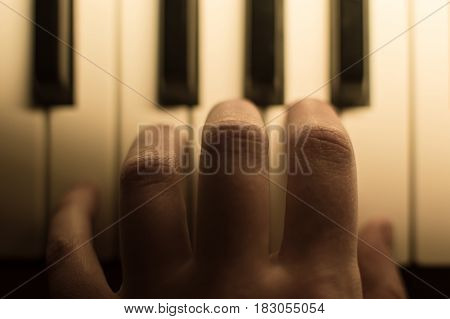Close-up toned atmospheric photography of a hand playing the piano. Concept: Music creating, composing, lyrics