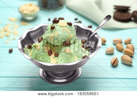 Tasty pistachio ice cream in bowl and nuts on wooden table