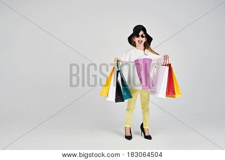 Little girl is wearing oversized hat and shoes. She is opening a purple shoppers bag. Girl has a surprised emotion on her face. Shopping, purchases, buy, sale concept