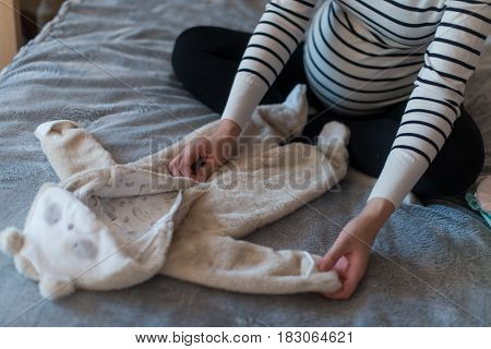 Pregnant woman dreaming and holding baby's clothes.