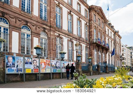STRASBOURG FRANCE - APR 23 2017: Black ethnicity man and caucasian woman admiring official campaign posters for all eleven candidates for the 2017 French presidential elections posted outside a polling station at City Hall pooling station