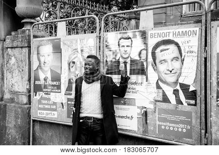 STRASBOURG FRANCE - APR 23 2017: Black ethnicity man showing his support to Emmanuel Macron near all 11 presidential posters - black and white image