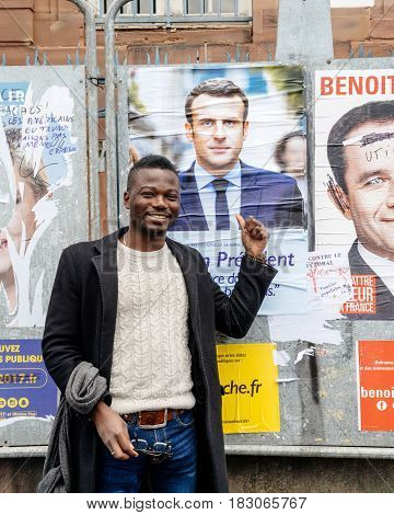STRASBOURG FRANCE - APR 23 2017: Black ethnicity man showing his support to Emmanuel Macron near all 11 presidential posters