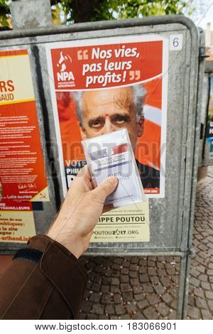 STRASBOURG FRANCE - APR 23 2017: French voter registration card held by male hand in front of official campaign poster of Philippe Poutou candidate for the 2017 French presidential elections posted outside a polling station