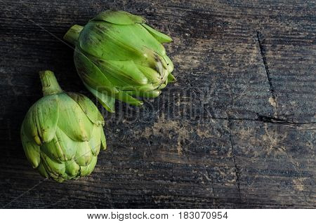 Two ripe fresh organic artichokes on rustic wooden background with place for text. Top view. Copy space.