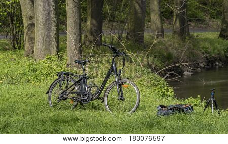 Electric bicycle with backpack and tripod in green spring grass