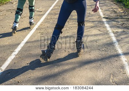 Two girls ride on rollers on a very bad road. The fallen branches lie on the asphalt. Extreme rollerskating. View of legs.