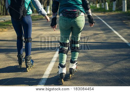 Two girls on roller skates ride along the road next to each other. Sport girls. View of legs.