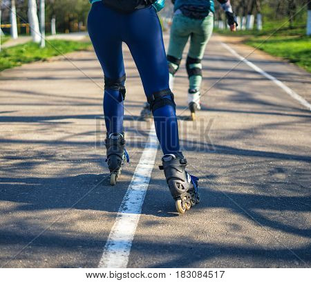 Competitions in roller skating. Two girls on roller skates ride along the road . Sport girls. View of legs