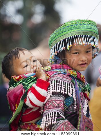 Sa Pa, Vietnam - March 15, 2017: Unidentified Hmong girl carrying baby and wearing traditional attire in Sapa, North Vietnam