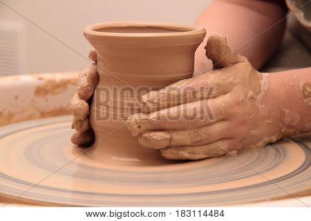 hands of a potter, creating an earthen jar on a pottery wheel