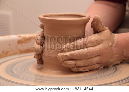 hands of a potter, creating an earthen jar on a pottery wheel