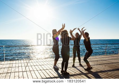 Silhouettes of young beautiful sportive girls giving highfive near sea at sunrise.