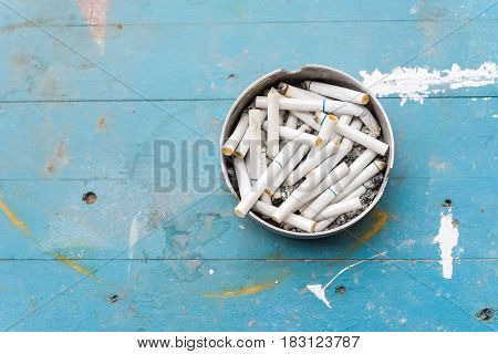 Various cigarette butts in dirty full ashtray