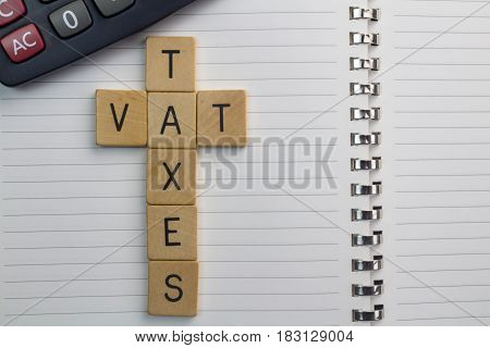 Accounting / Finances background - Taxes and VAT words on scrabble blocks with notepad and calculator