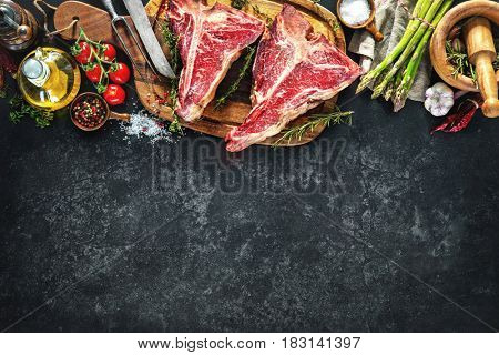 Raw dry aged t-bone steaks for grill with fresh herbs and vegetables